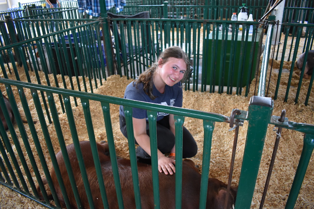 An FFA student smiling at the camera with her pig inside of the pig's pen at the fair
