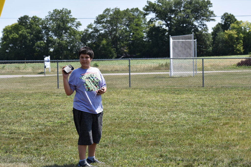 A student standing in the grass and looking back toward the camera while holding his phone in his hand