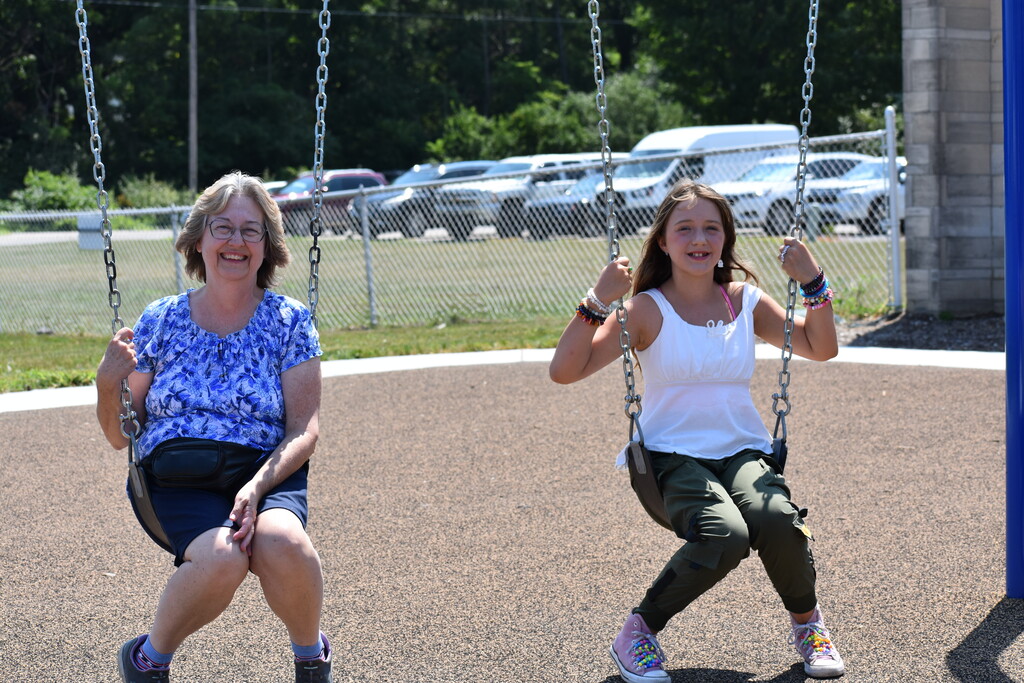 A parent and student swinging on swings and smiling at the camera