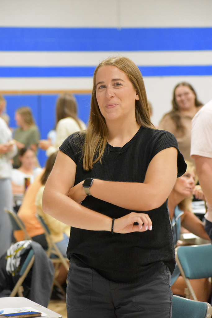 An LISD staff member crossing her arms and smiling at the camera while standing among her peers in the gymnasium