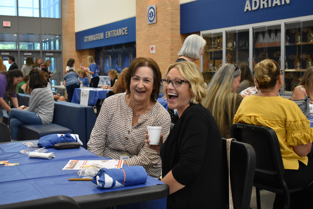 In a crowded space, two people smile at the camera from their seats at a table
