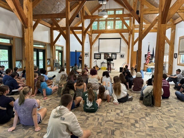 A view from the back of the room where JC LISD Academy students are seated on the floor and a presenter is speaking to them from the front