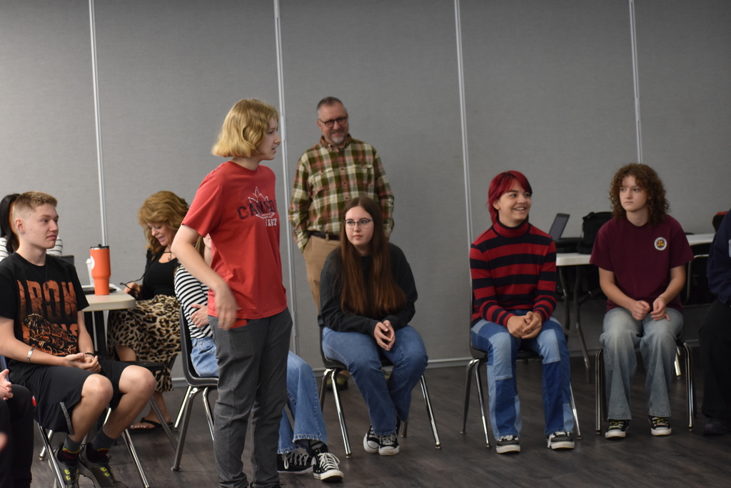Students seated in a circle and one student standing up in the middle of the circle