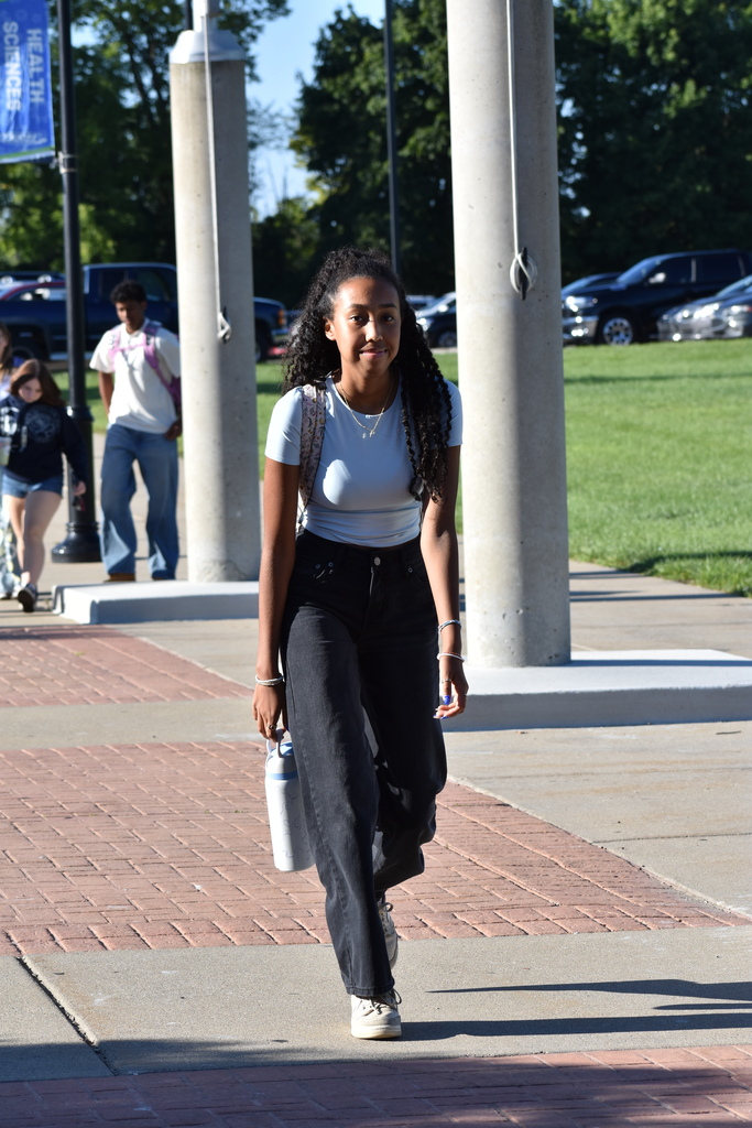 A student smiling at the camera as she walks toward the building 