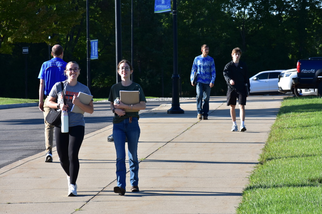 Four students walking down the sidewalk toward the building