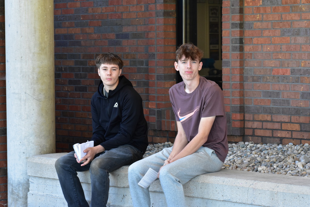 Two students seated outside the building and looking at the camera 