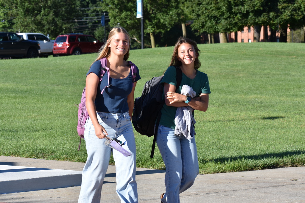 Two female students smiling at the camera as they walk toward the building 