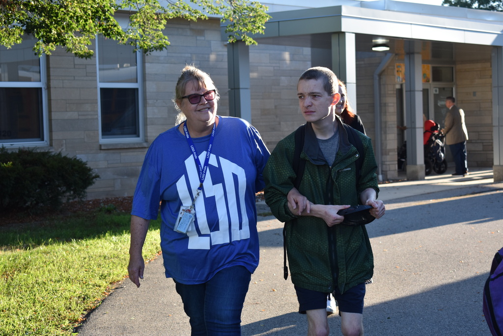 A teacher and student walking arm in arm outside of the school building