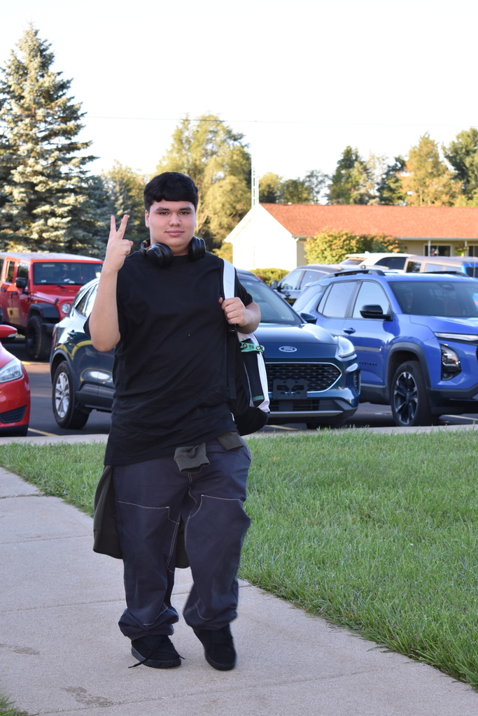 A student throwing up a peace sign as he walks toward the building