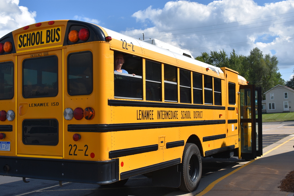 An LISD school bus with a driver looking out the back window