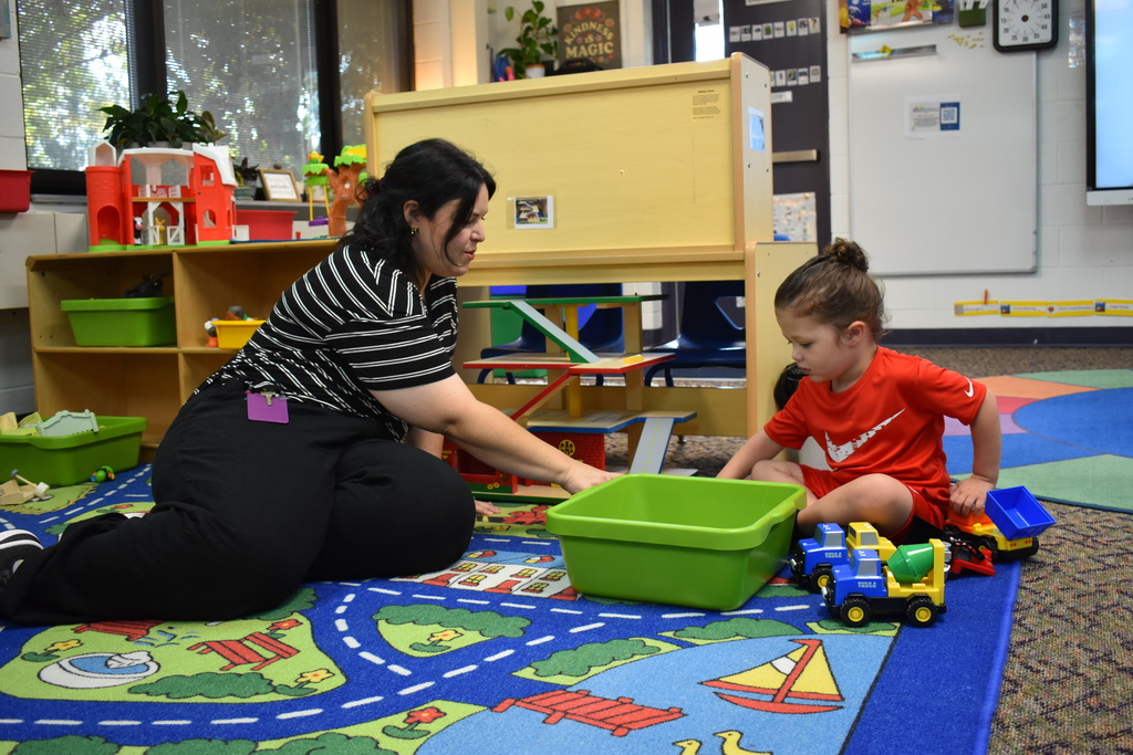 A new student and teacher on the floor playing with trucks