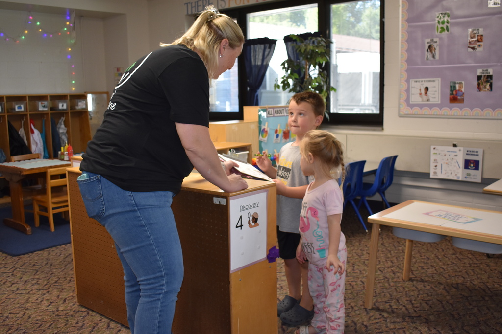 A mom looking at her two children as the new student explores his classroom