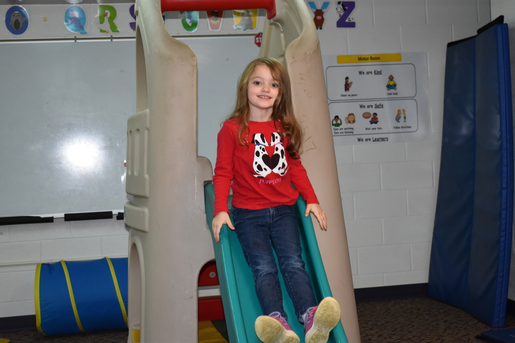 A new student coming down an indoor slide and smiling at the camera