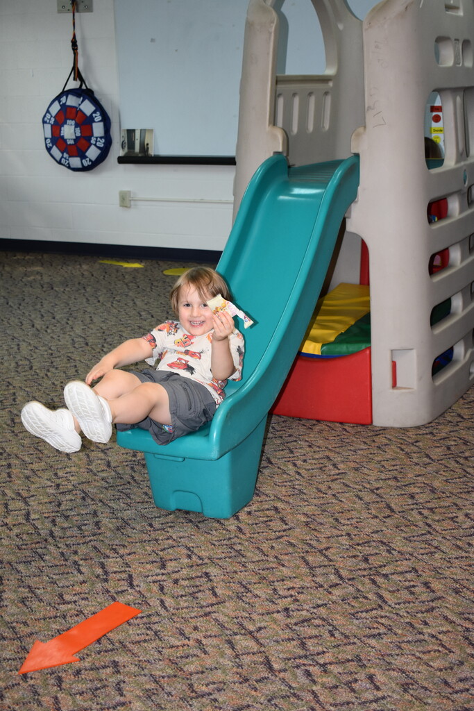 A young student coming down an indoor slide and smiling