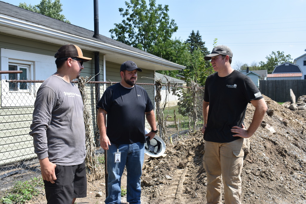 Three guys standing and talking to each other at the house site
