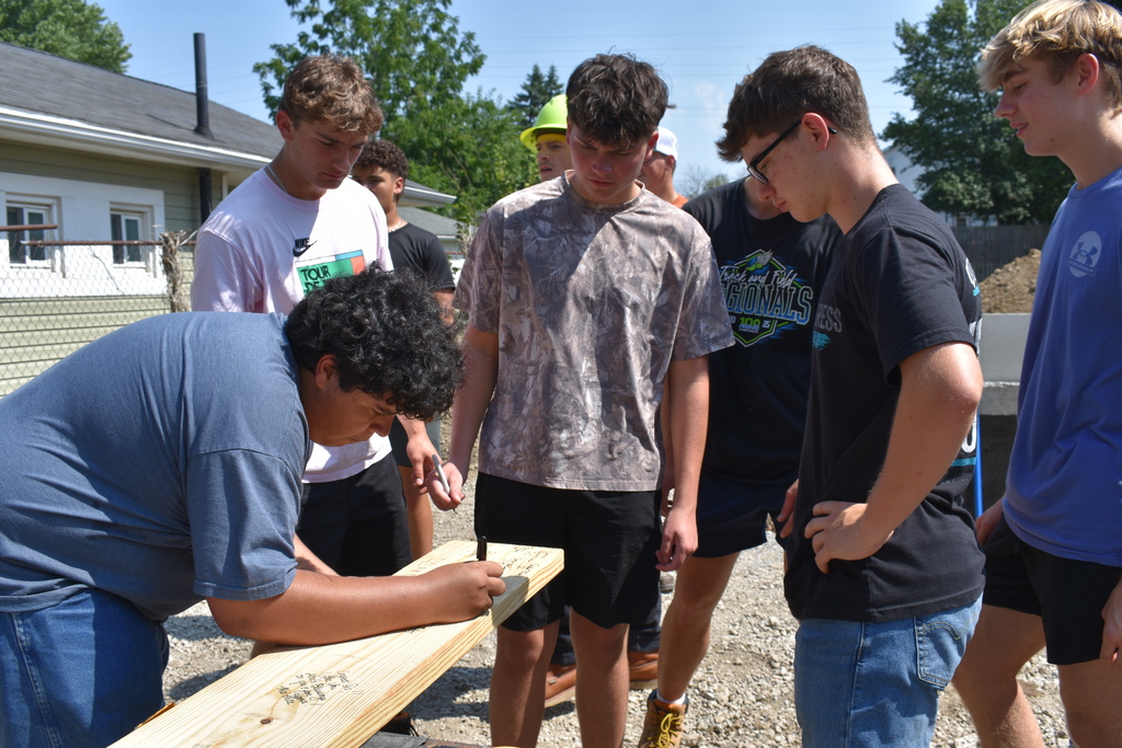 A student signing a board as the other students look on
