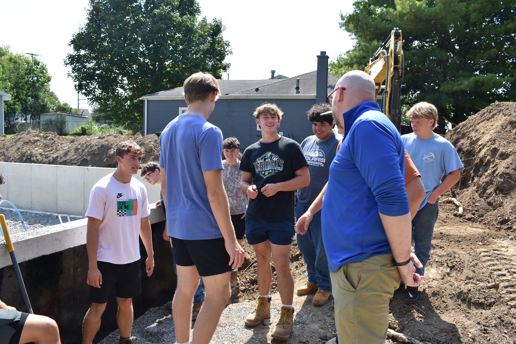Students smiling and laughing at the principal who walked up to talk to them as they stand around at the new site