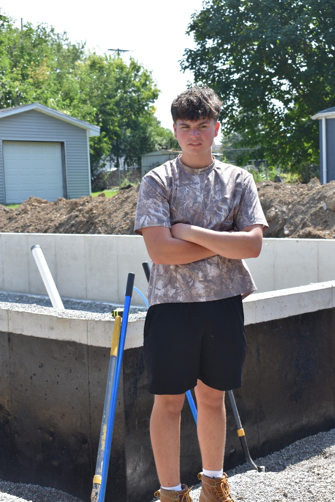 A student standing near the poured foundation of the new home