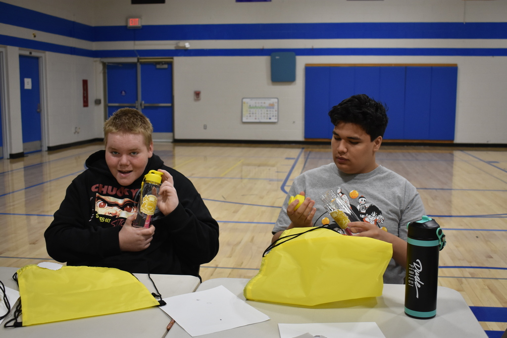 A student smiling with a prize as another student looks at his