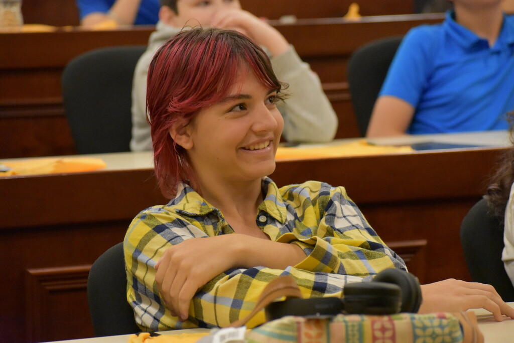 A student smiling at a presenter from her seat while sitting in an auditorium