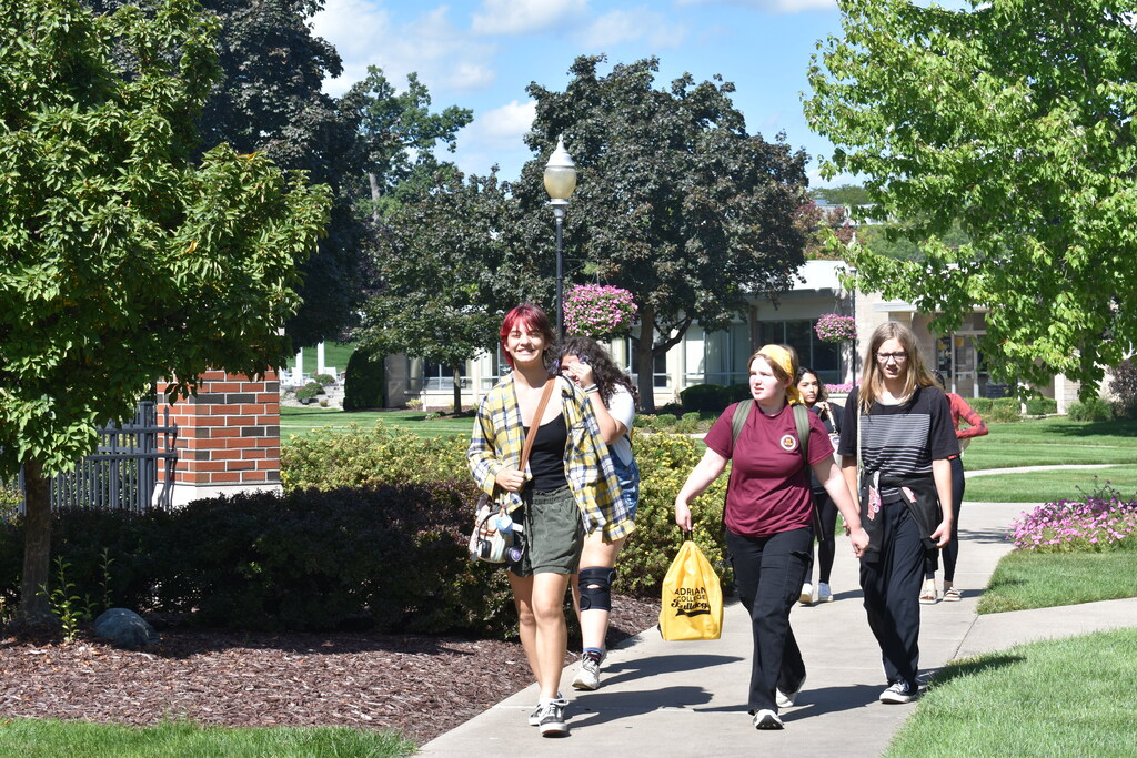Students walking across campus, all facing the camera, as one smiles to the camera for the photo