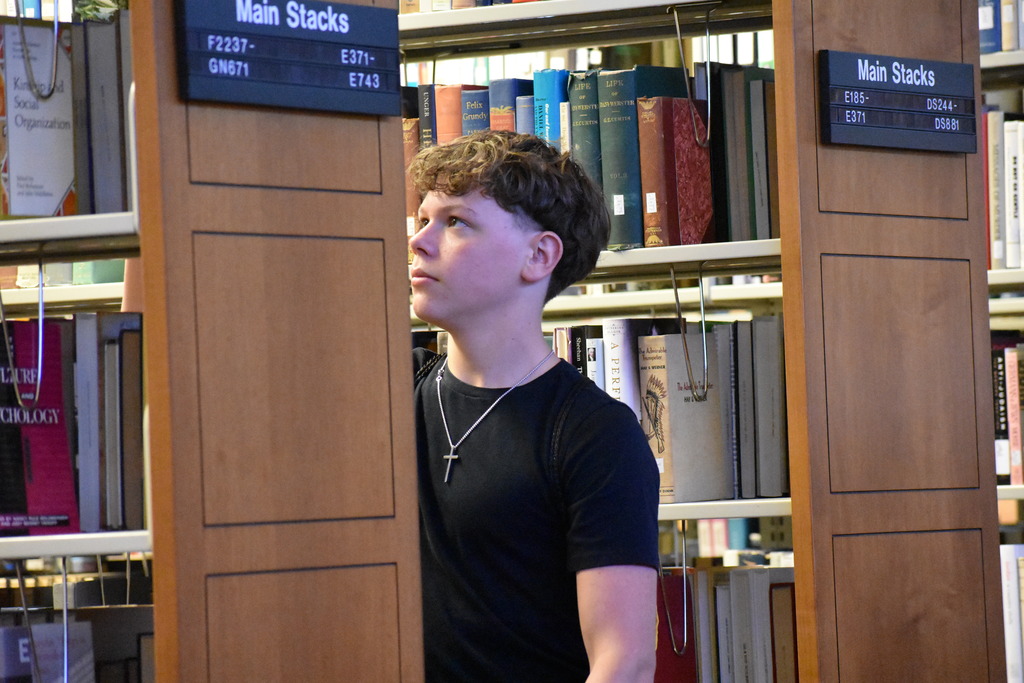 A student touring the library standing in between book rows and looking at a book