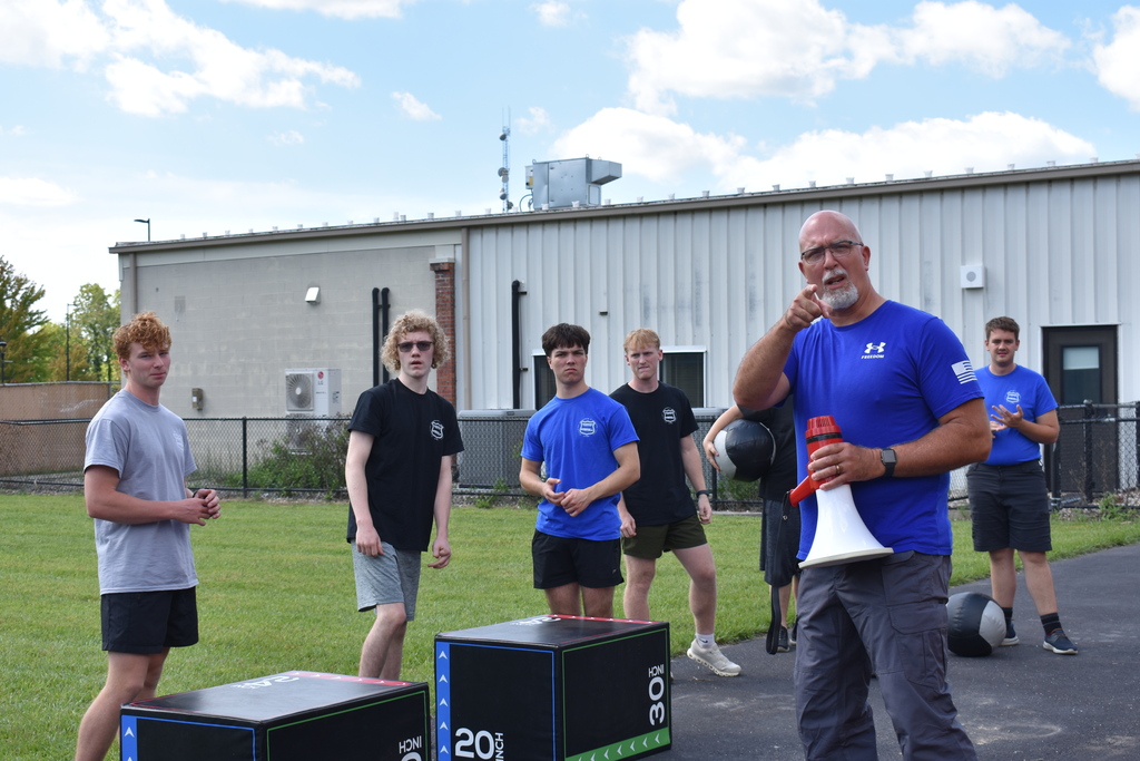 Instructor McMullen pointed at a board while students stand around and prepare for a workout