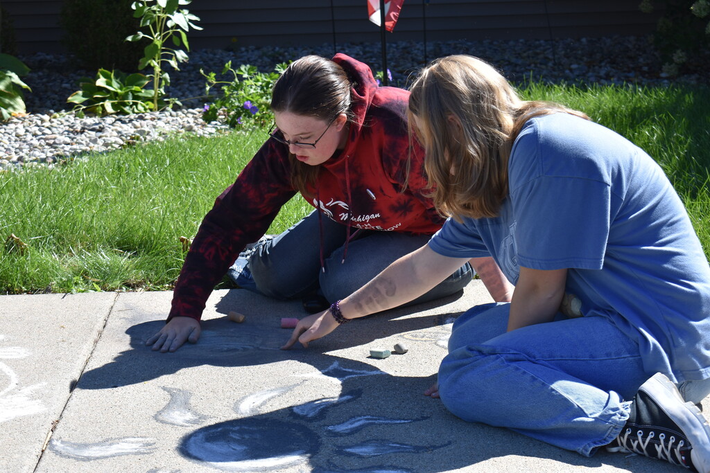 Two students working on their sidewalk chalk art while seated on the ground.