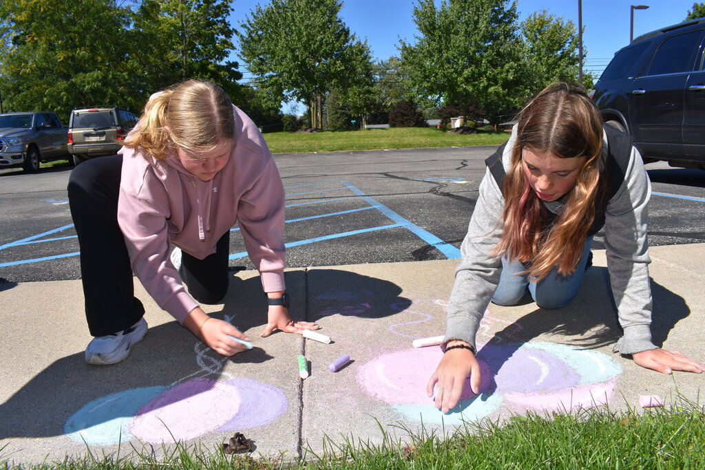 Two students cleaning up some art work on a sidewalk using their hands and chalk