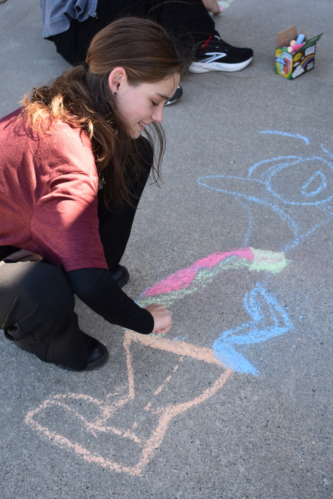 A female student kneeling down working on a design with sidewalk chalk.