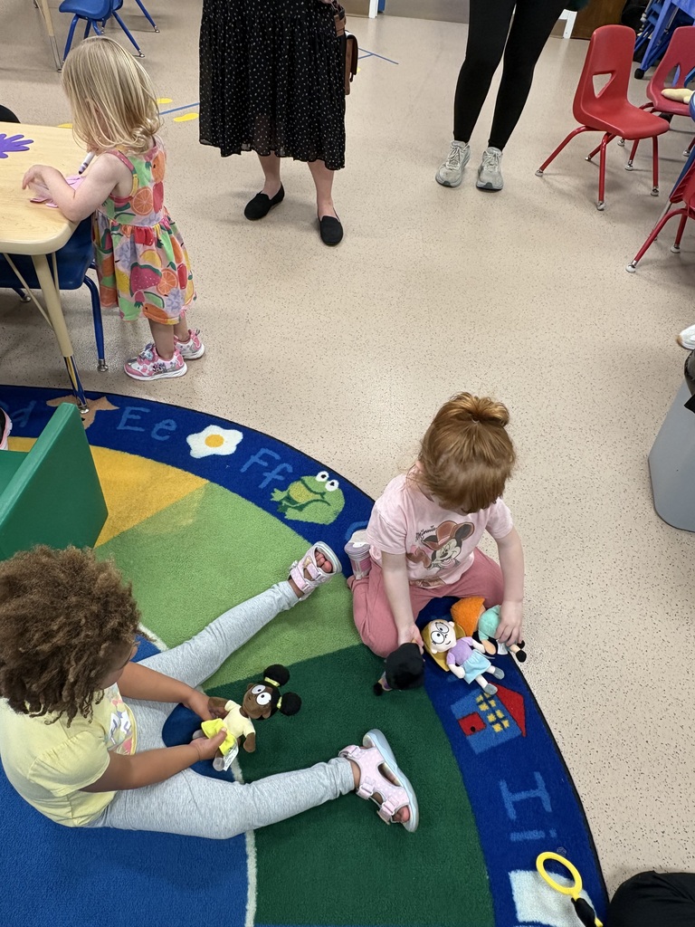 Two girls playing at the carpet with dolls.