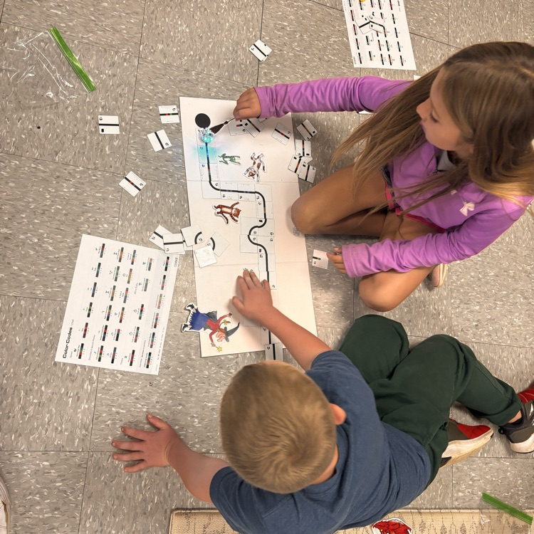 students sit on the ground with a white mat, ozobot, and book characters