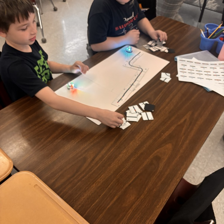 students sit at a table with a white mat, ozobot, and a magnetic path