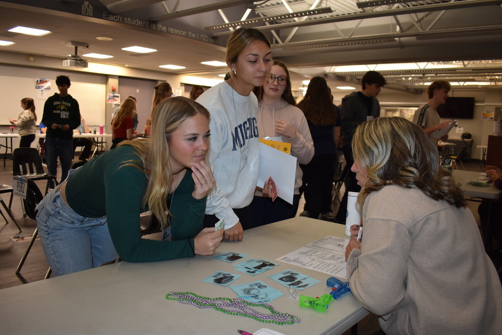 Students gather around a table to speak with a volunteer while navigating simulated financial decisions and community resources.