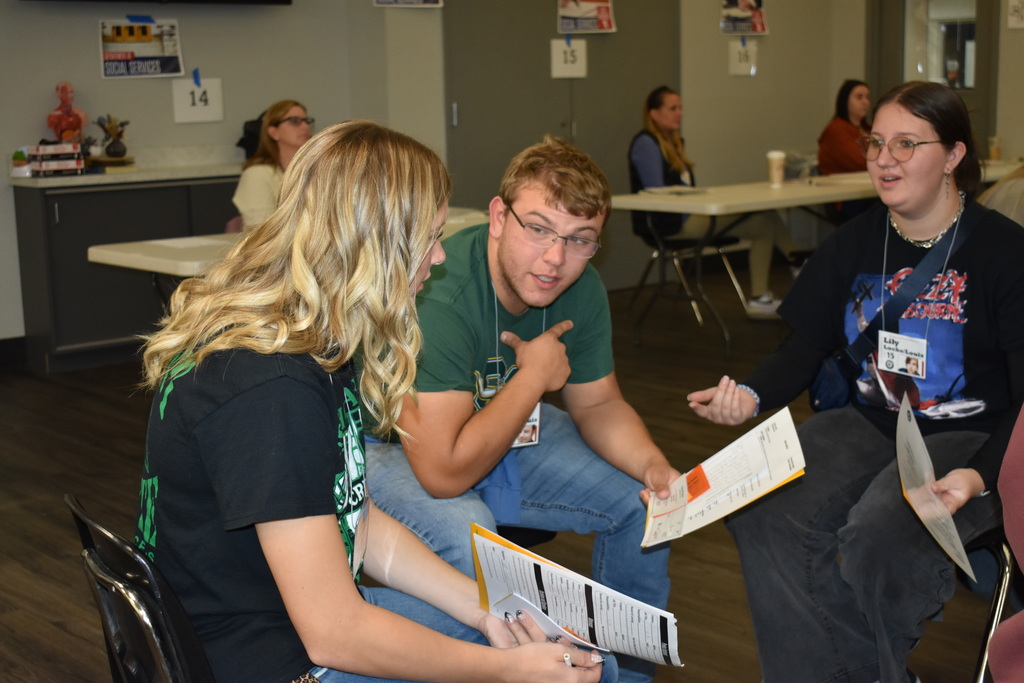Three students sit together discussing paperwork and making decisions as part of the Poverty Simulation.