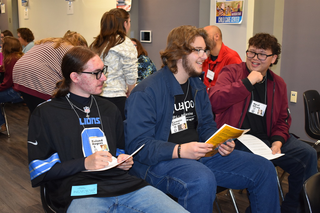 Three students sit together reviewing information sheets and discussing their assigned scenarios during the Poverty Simulation.