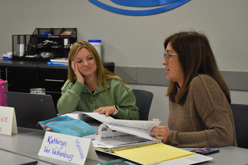 Two educators engage in conversation while reviewing instructional resources and literacy materials during the training session.