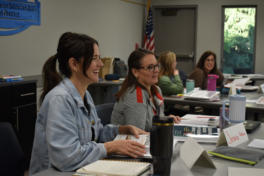 Two educators smile and participate in a group discussion with fellow teachers during the Secondary Literacy Network training.