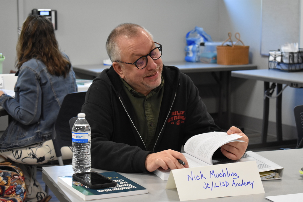 An educator from JC/LISD Academy reviews an open book during the Secondary Literacy Network training, with instructional materials spread across the table.