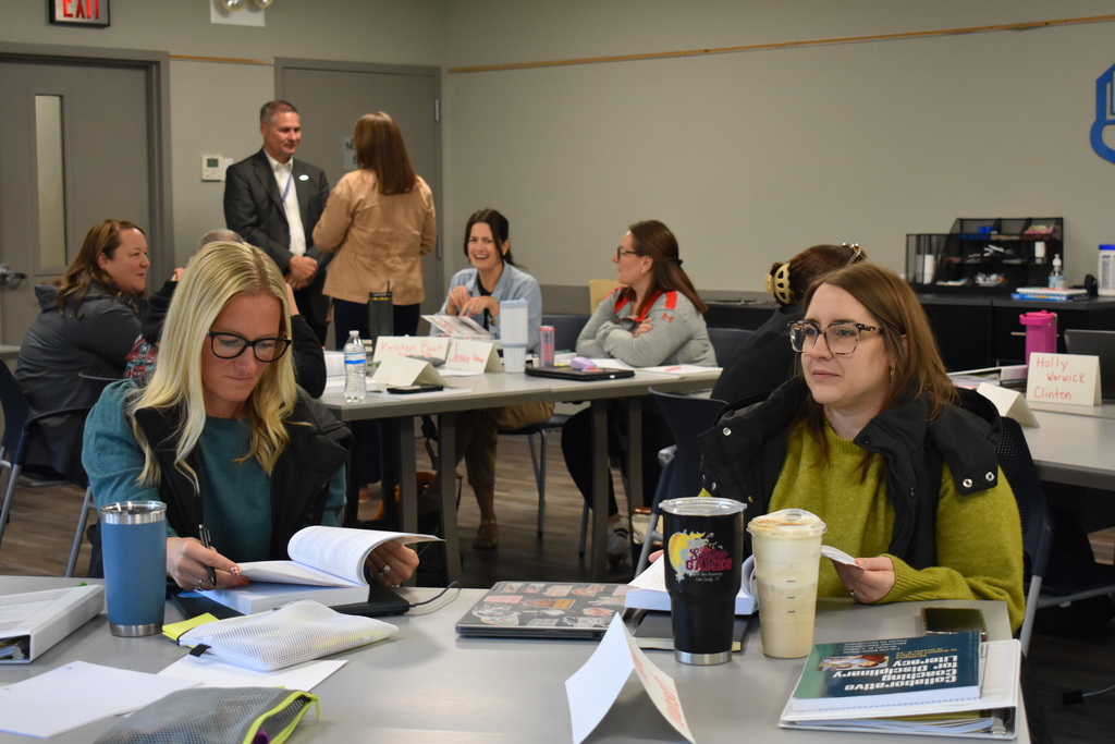 Lenawee County educators participate in a Secondary Literacy Network training session, reviewing materials, taking notes, and engaging in conversations around tables.