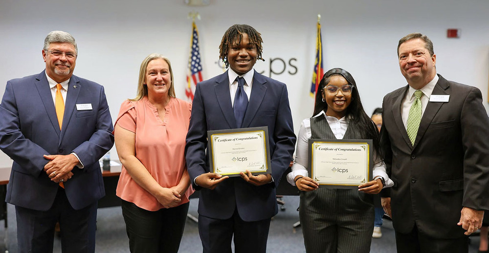 Two African American high school seniors pose with certificates recognizing their winning scholarships.