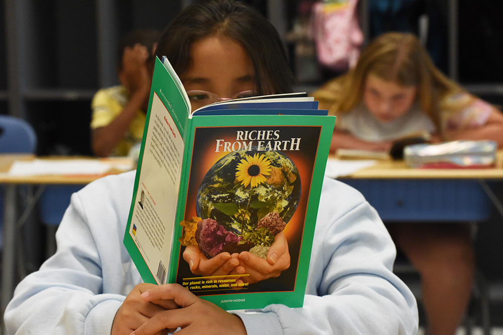 Elementary age girl has her face buried in a book.