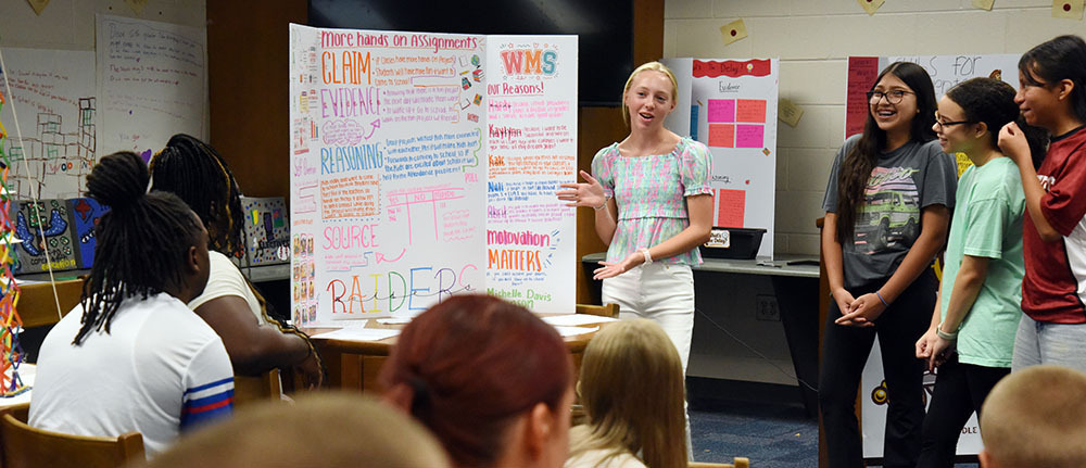 Four eghth-grade girls use a hand-designed poster to explain their work on an assignment.