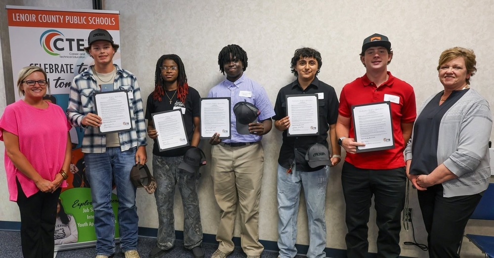 New interns for Crown Equipment stand with signed papers and hats at 2nd annual signing day