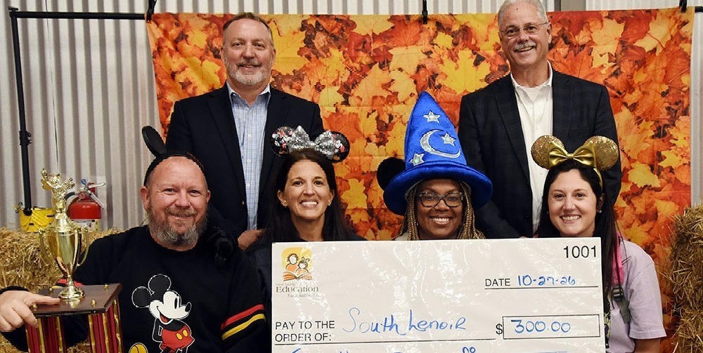Four adults in Disney costumes display a carboard check while two men pose behind them.