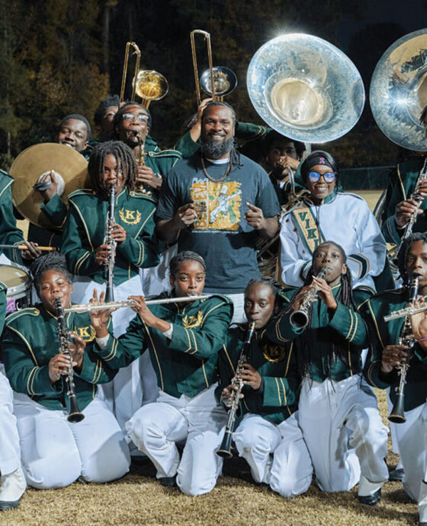 High school band members in green and white uniforms pose with their instruments.