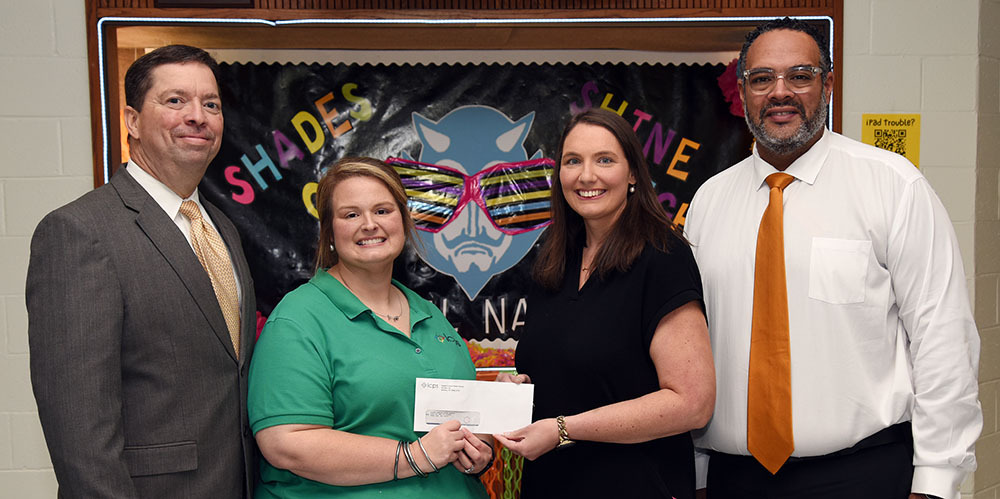 Four people pose with two holding a check.
