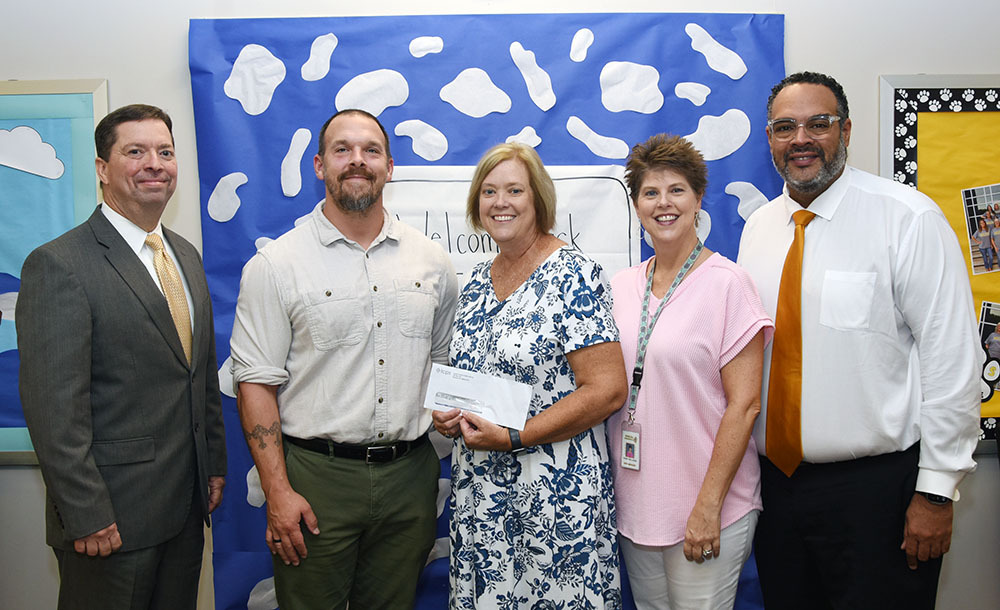 Five people pose with ne holding a check.