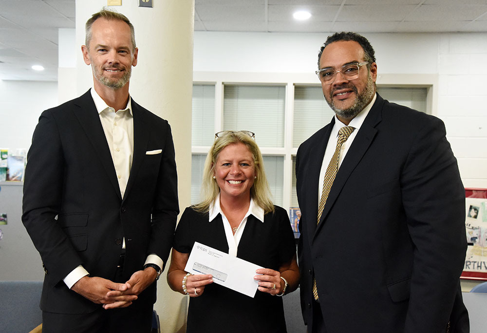 Three peoiple pose with one holding a check.