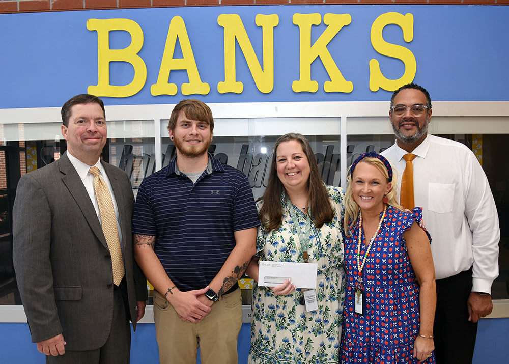 Five people pose with one holding a check.